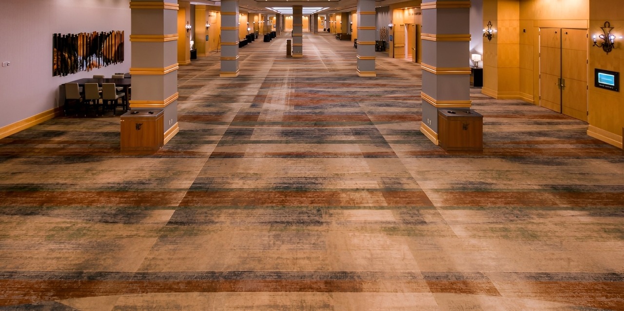 Spacious Convention Center Hallway With Patterned Carpet and Lit Wooden Doors, Ideal for Events and Gatherings.